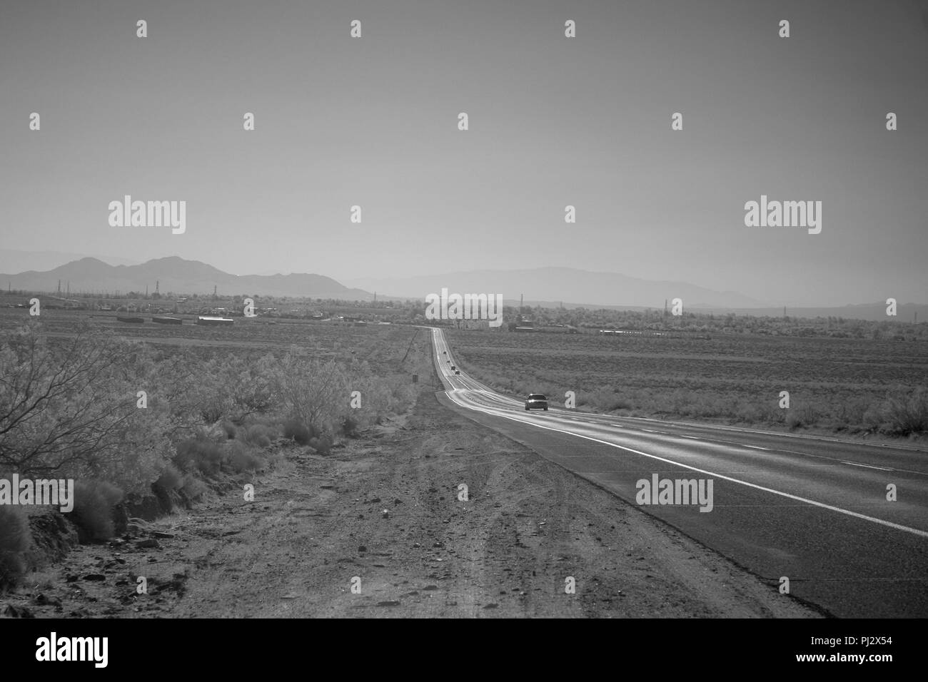 Ein einsamer Wüste Highway hinunter in ein Tal mit Dunstige Berge. Stockfoto