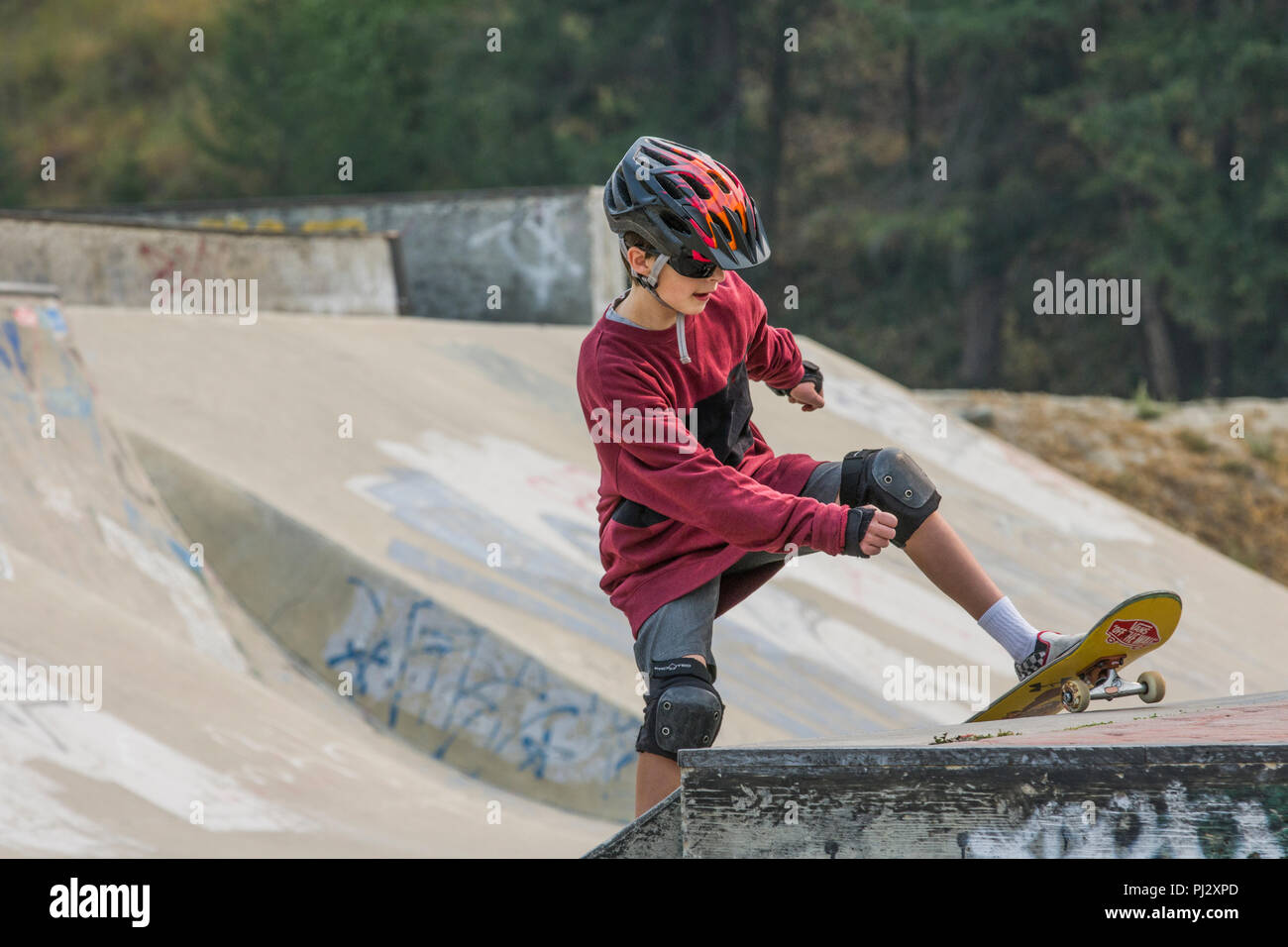 Jung, 12 Jahre alt, hübsches Kind, das Tragen von Skateboard Ausrüstung und Skateboarden. Bunte Helme, Knieschoner, Ellenbogenschützer, Shorts, Model Released Stockfoto