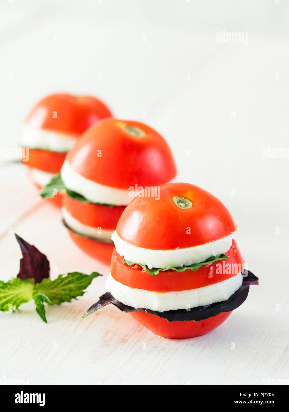 Ready-to-Spaß Essen layered appetiezer mit Tomaten, Käse, lila Basilikum, Minze. Ideen und Rezepte für ein gesundes Frühstück, Abendessen, appetiezer, Salat. Kann für Design Käserei verwenden. Platz kopieren. Vertikale Stockfoto