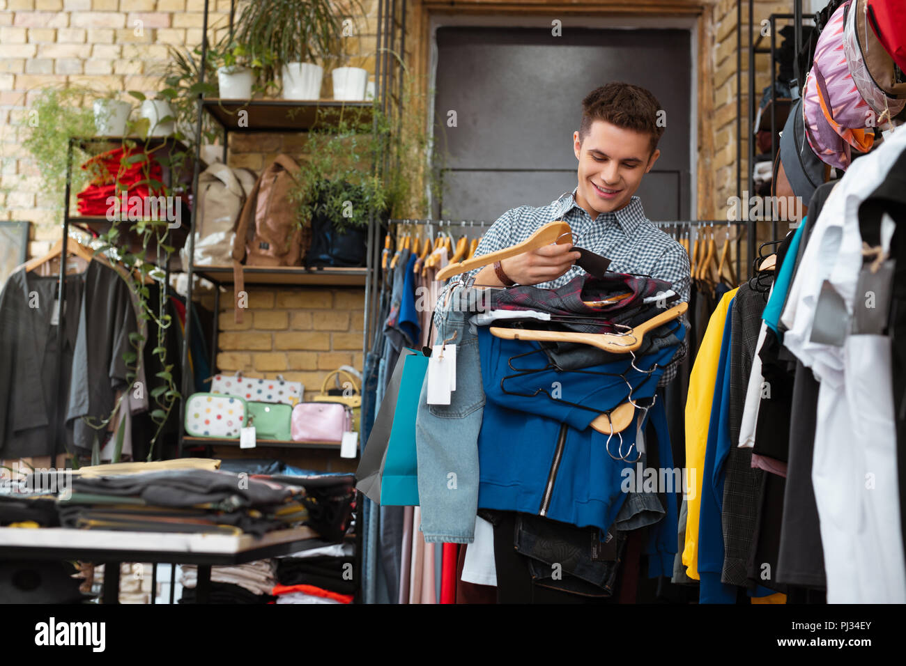 Positive junger Mann und lächelnd große Menge Kleider auf Kleiderbügeln Stockfoto