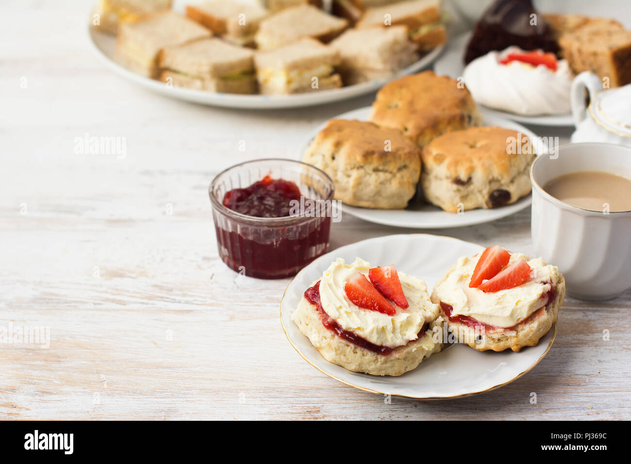 Englisch Cream Teas, Scones mit Marmelade und Sahne, Tee mit Milch, mit Sandwiches auf der Rückseite, auf die Weiße Holztisch, selektiver Fokus kopieren Platz für t Stockfoto
