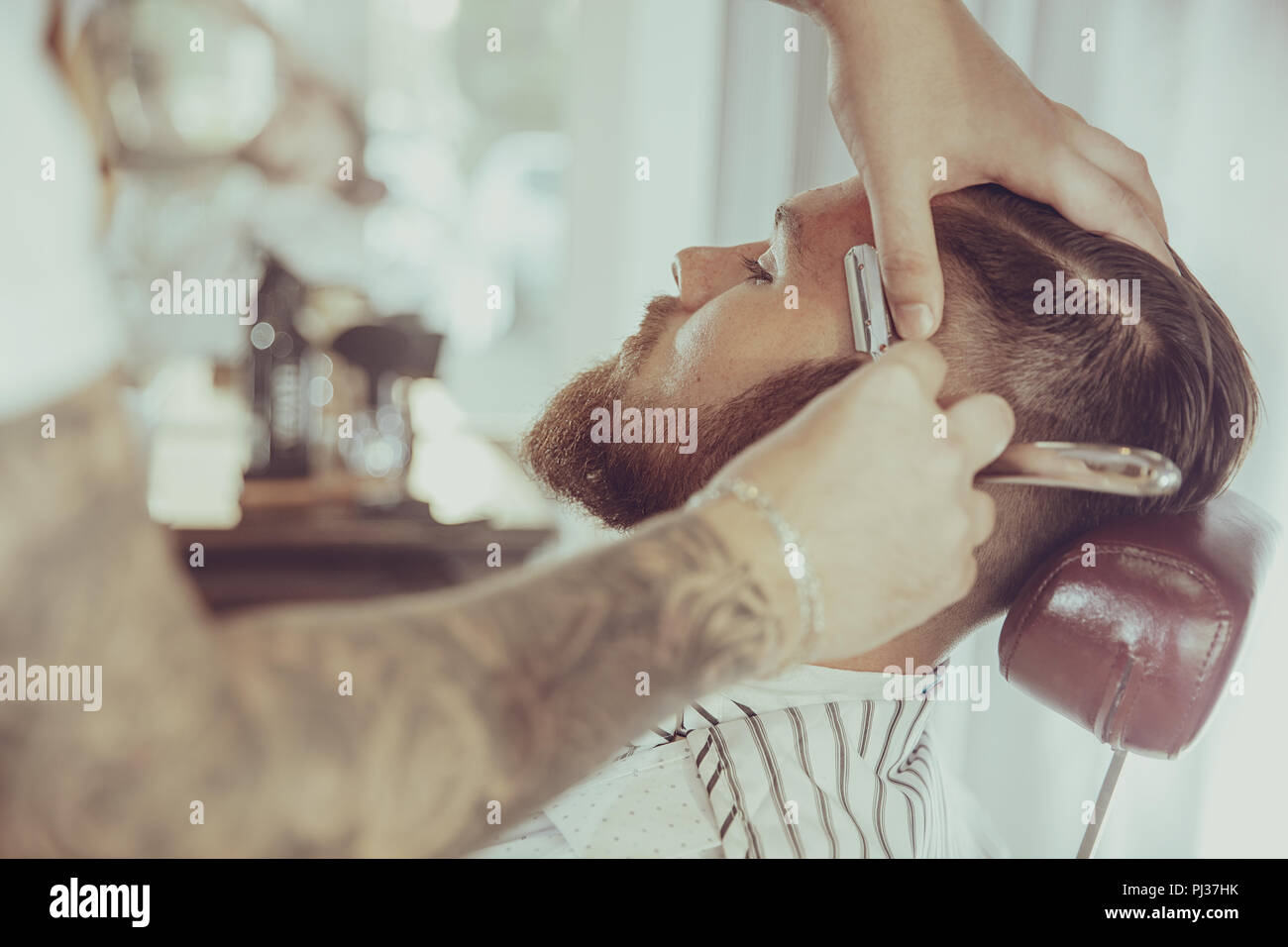 Mann mit einem Bart ist die Rasur mit einem Rasiermesser in einem Friseursalon. Foto im Vintage Style Stockfoto