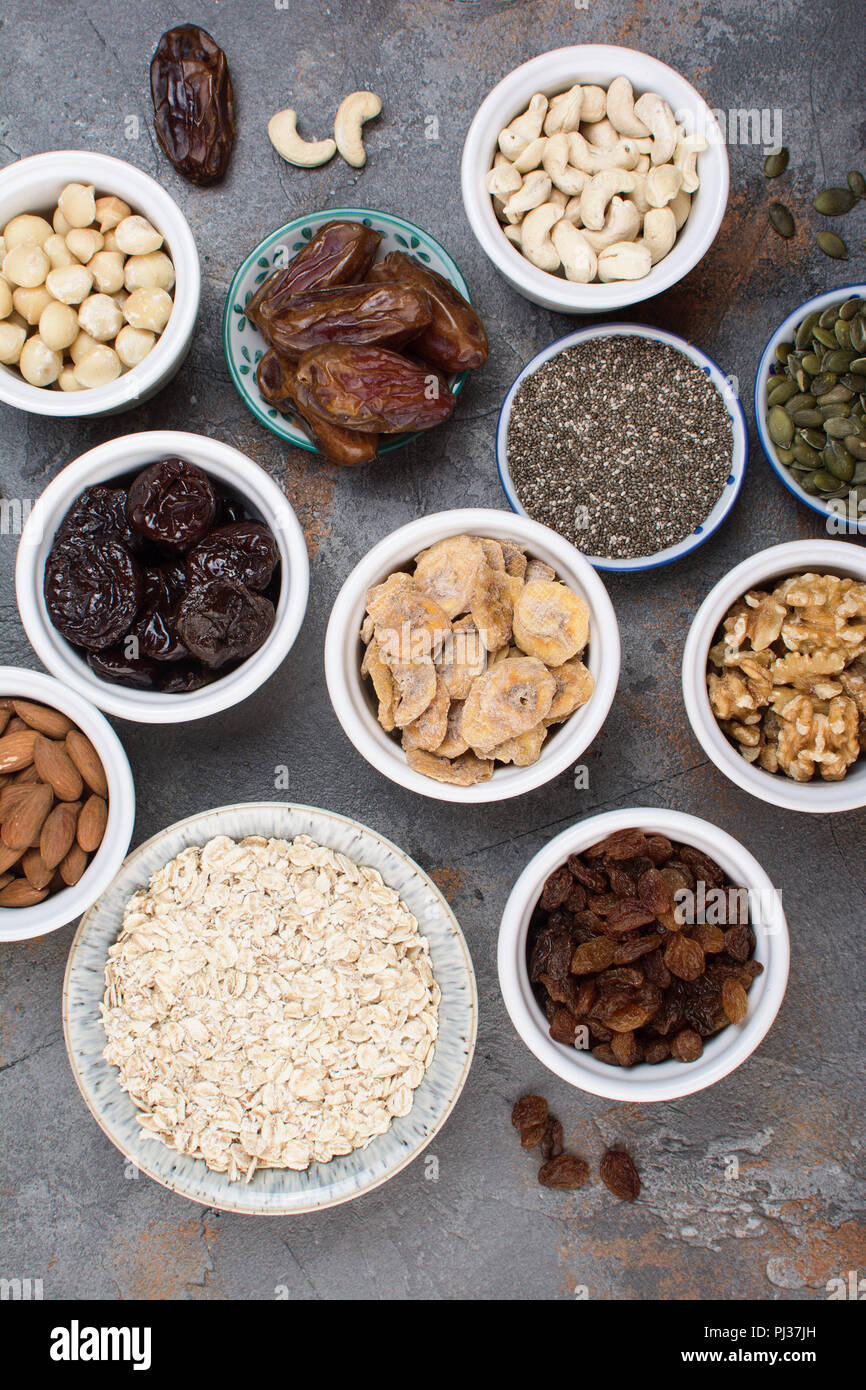 Oben Ansicht von Zutaten für hausgemachtes Müsli, Hafer, verschiedene Nüsse und Rosinen, Datteln, Samen auf dem grauen Stein Hintergrund, selektiver Fokus Stockfoto