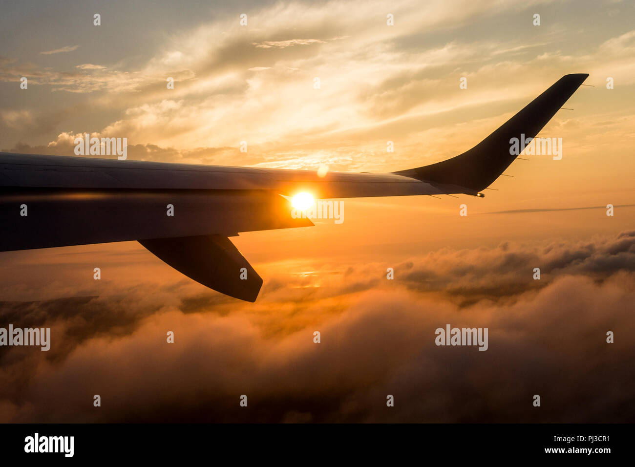 Sun durch ein flugzeugflügel aus dem Fenster einer Charter Flug mit einem orangefarbenen Sonnenuntergang Himmel gesehen Stockfoto