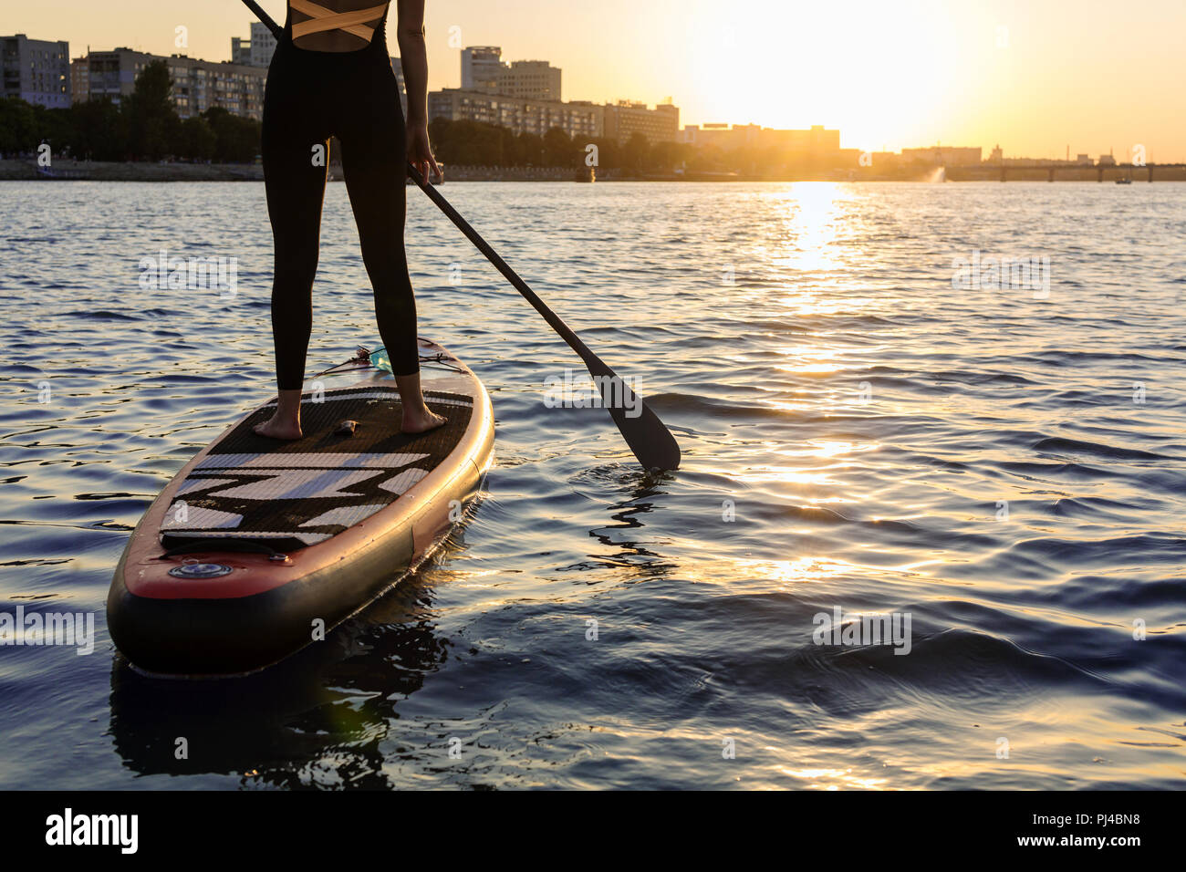 Frau mit einem Paddel an die Tafel. die Beine einer schlanken Mädchen auf Stand up Paddle Board. Stockfoto