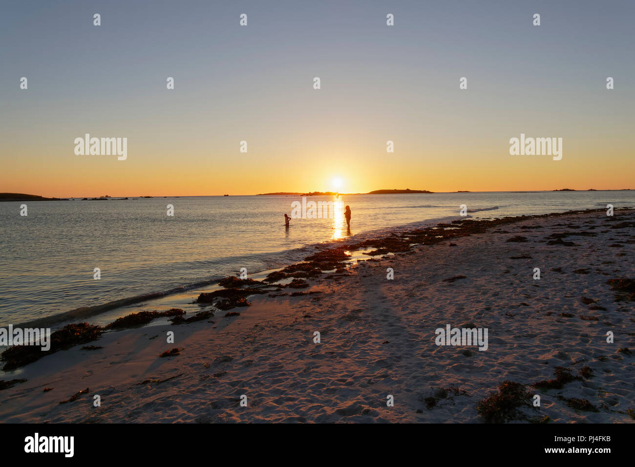 Wie die Sonne über Plage Sainte-Marguerite, Bretagne, zwei Menschen eine letzte Paddel in der Keltischen See. Stockfoto