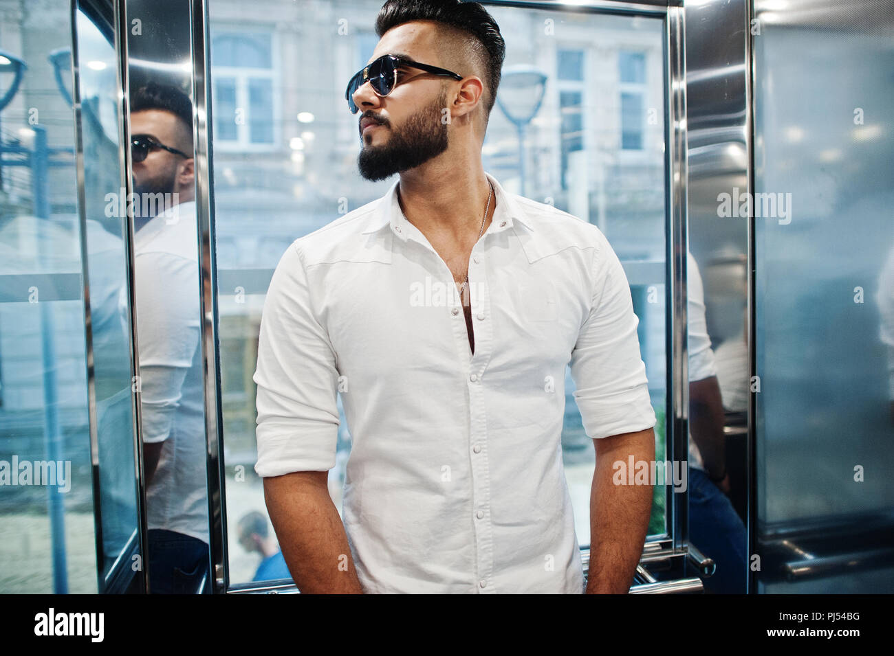 Stilvolle hohen arabischen Mann im weißen Hemd und Sonnenbrille bei Elevator innen gestellt. Stockfoto