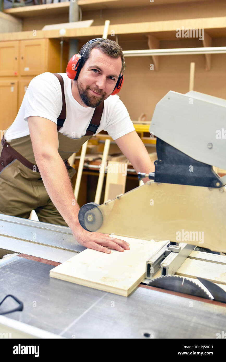 Freundlich Tischler mit Gehörschutz und Arbeitskleidung arbeiten an einer Säge in der Werkstatt Stockfoto