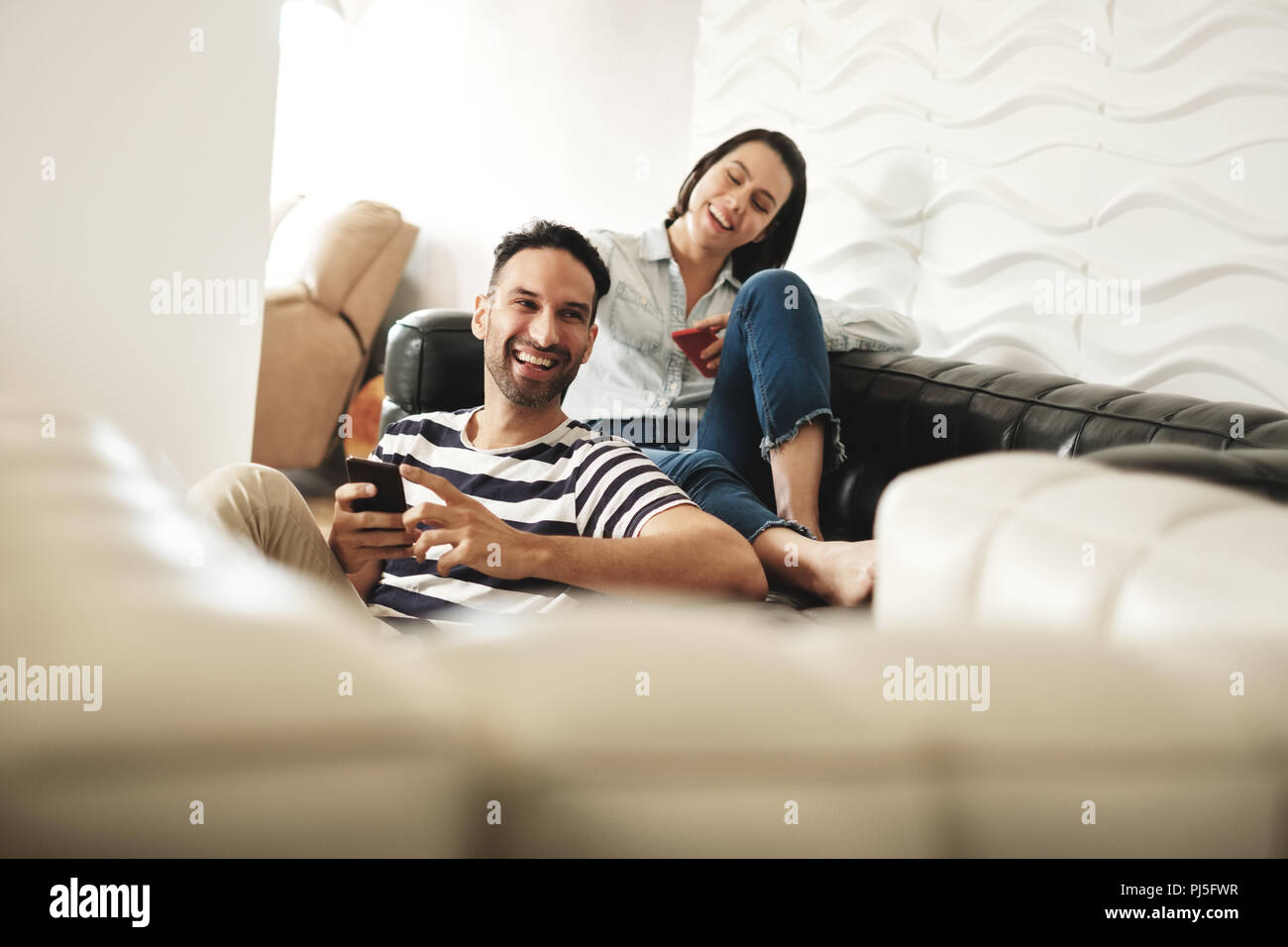 Jungen Latino Mann und Frau Messaging mit Mobiltelefonen auf dem Sofa zu Hause. Happy hispanic Paar mit Handys. Menschen mit Smartphones Stockfoto