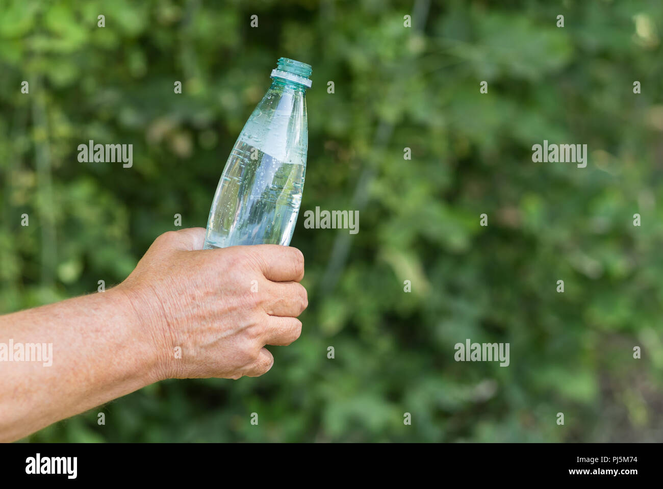 Hand, denn der Mann öffnete eine Flasche Mineralwasser gegen grüne natürlichen Hintergrund Stockfoto