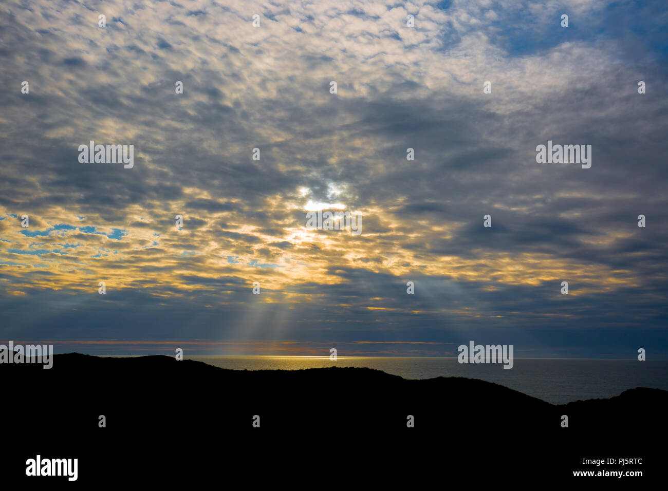 Abendlicht, mit Meerblick von Silhouette Landspitze letzten Strahlen der Sonne nach unten durchgebrochen Cloud Beleuchtung bis aufs Meer. Sonne über Horizont Stockfoto
