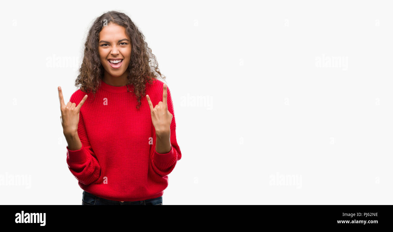 Junge Hispanic Frau das Tragen der roten Pullover schreien mit verrückten Ausdruck tun Rock Symbol mit hands up. Musik Star. Schwere Konzept. Stockfoto