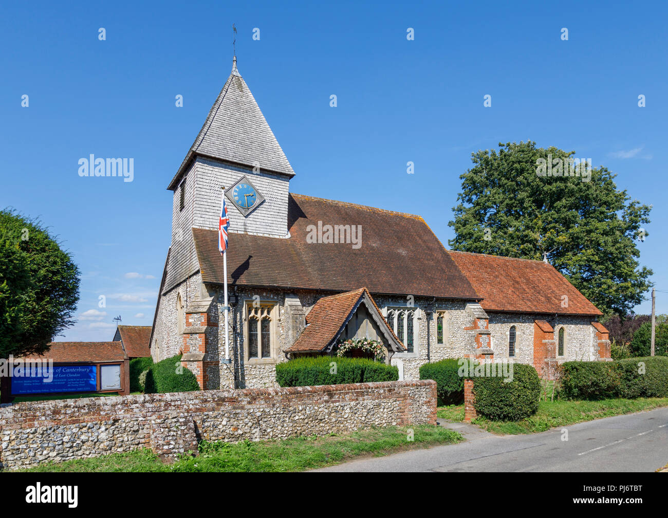 Am Straßenrand Blick auf Kirche des Hl. Thomas von Canterbury und seine Feuerstein Friedhofsmauer im East Clandon, einem kleinen Dorf in der Nähe von Guildford, Surrey, England Stockfoto