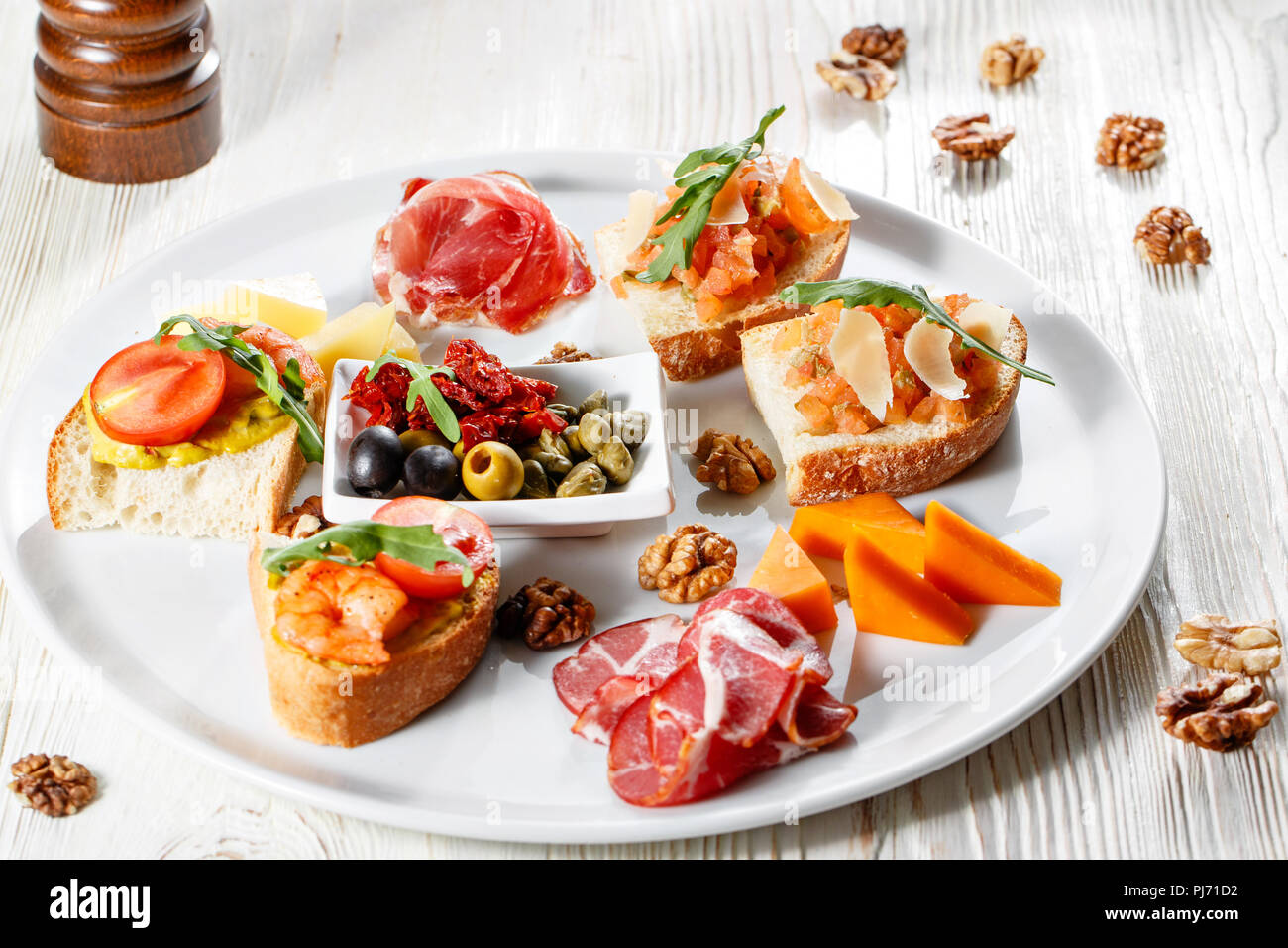 Mit italienischen Vorspeisen Teller. Bruschetta mit Tomaten und Garnelen. Parmesan Käse, Schinken, grüne Kapern, Oliven, sonnengetrockneten Tomaten und Walnüsse Stockfotografie
