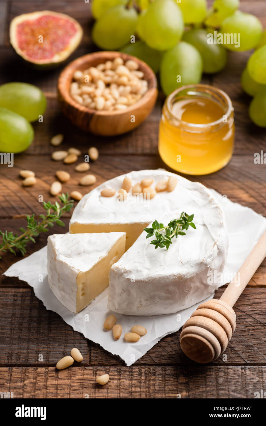 Brie oder Camembert mit Pinienkernen, Feigen, Honig und grüne Trauben auf braunem Holz- dienen. Detailansicht, selektiver Fokus Stockfoto