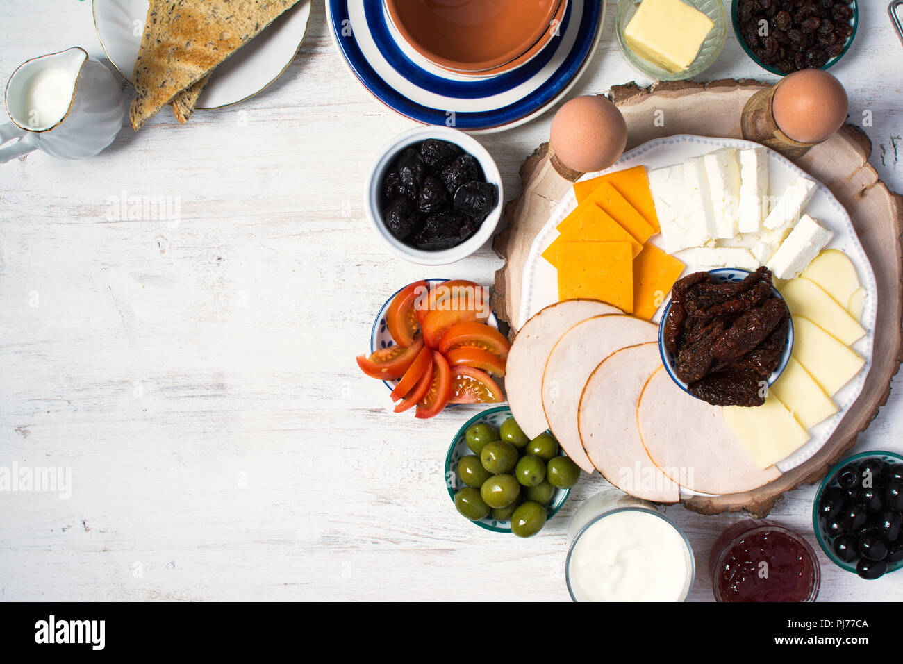 Gesunde und verschiedene Frühstück Auswahl: Eier, Oliven, Müsli, Schinken, Käse, Brot, Nüssen auf die weiße Holztisch, selektive konzentrieren. Ansicht von oben Stockfoto