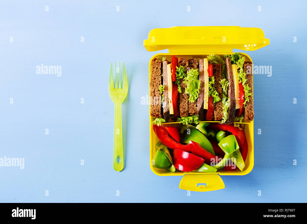 Gesunde Schule Lunch Box mit Rindfleisch Sandwich und frisches Gemüse auf blauem Hintergrund. Ansicht von oben. Flach Stockfoto