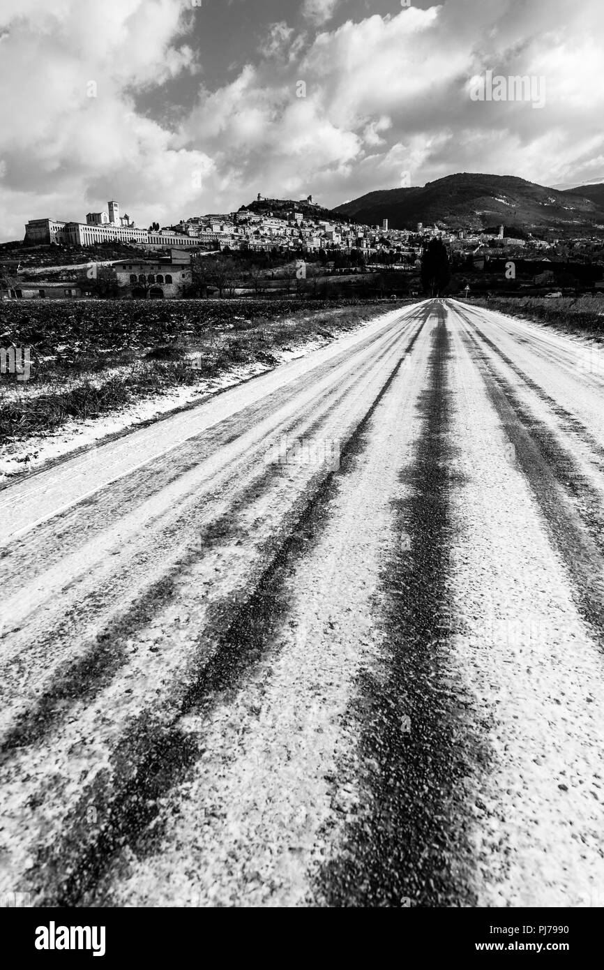 Blick auf die Stadt Assisi (Umbrien) im Winter, mit einem Feld durch Schnee und Himmel mit weißen Wolken bedeckt Stockfoto