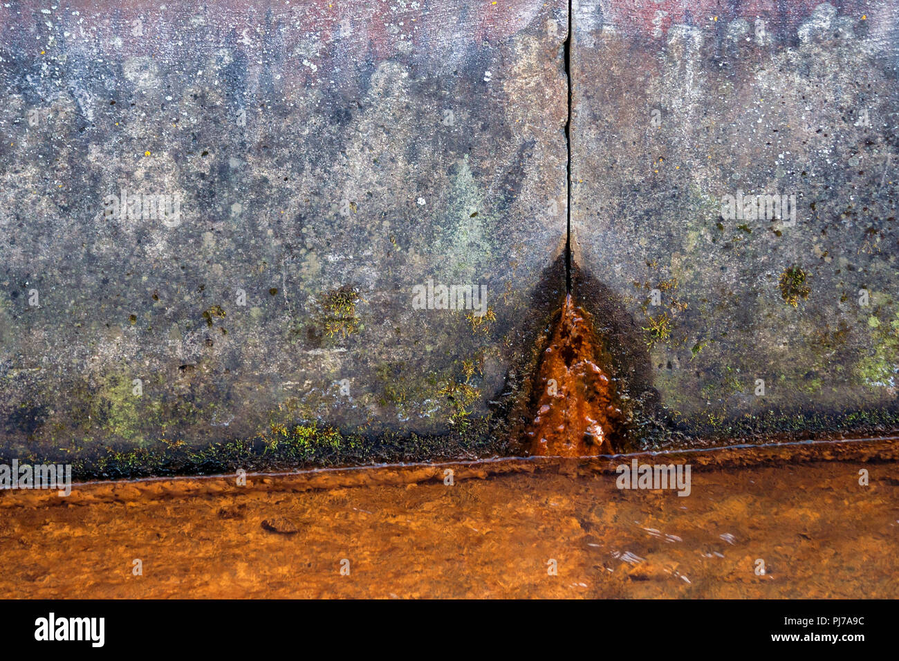 Zwei Betonplatten von schmutzig grauen Farbe in Spots, rostiges Wasser fließt aus dem Loch von unten, im Vordergrund Es ist ein flüssiges Rusty von Korrosion, Stockfoto
