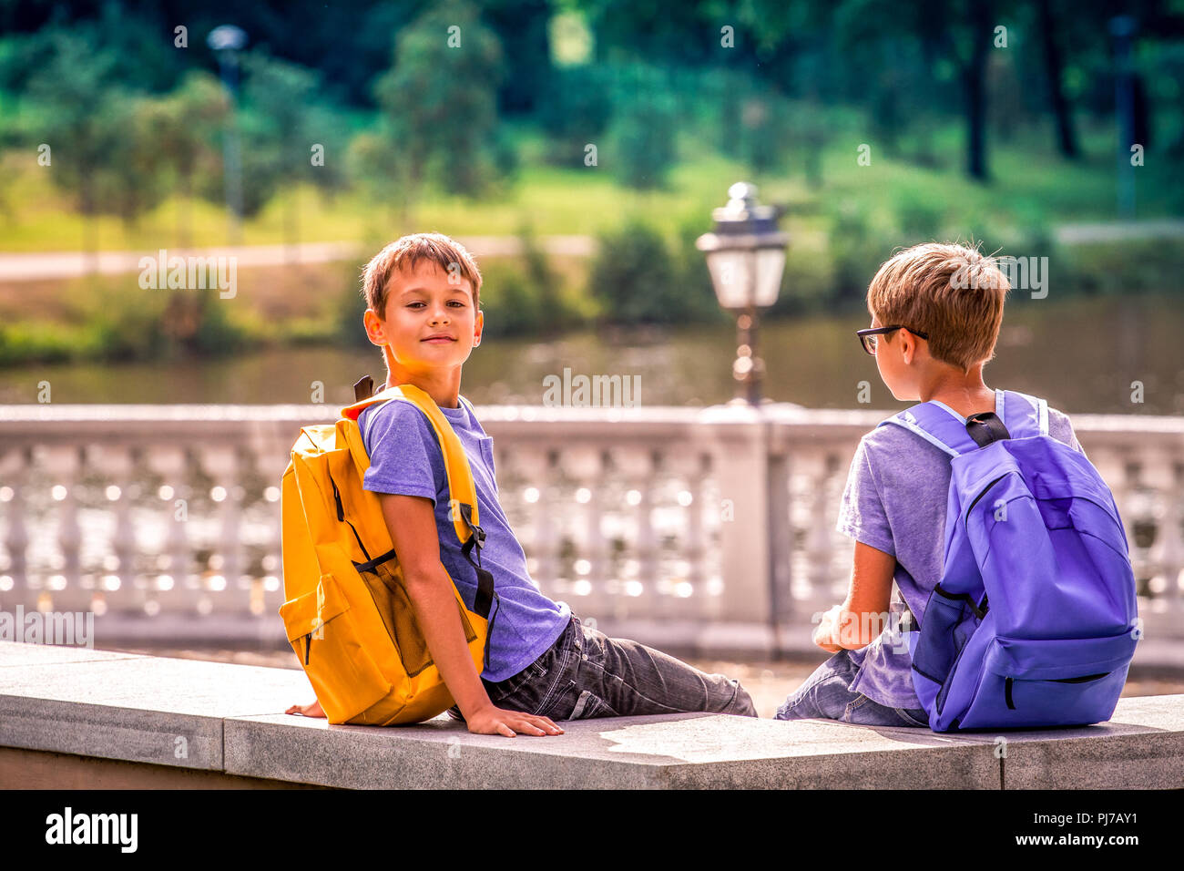 Grundschule, zurück zu Schule, Freundschaft, Kindheit, Kommunikation und Personen Konzept - Kinder mit Rucksack Sitzen im Freien. Stockfoto