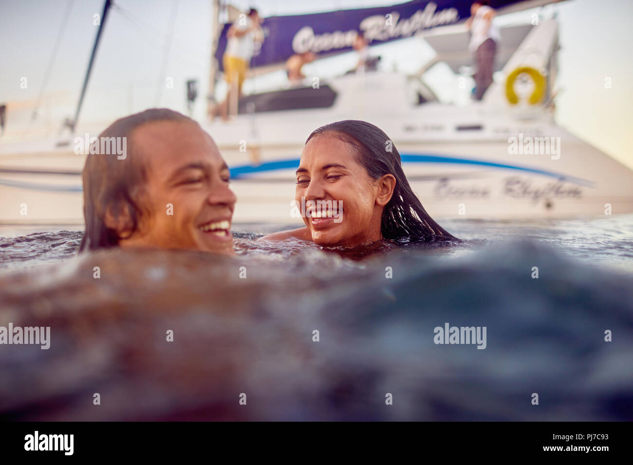 Glückliche junge erwachsene Paare schwimmen in der Nähe von Katamaran in Ocean Stockfoto