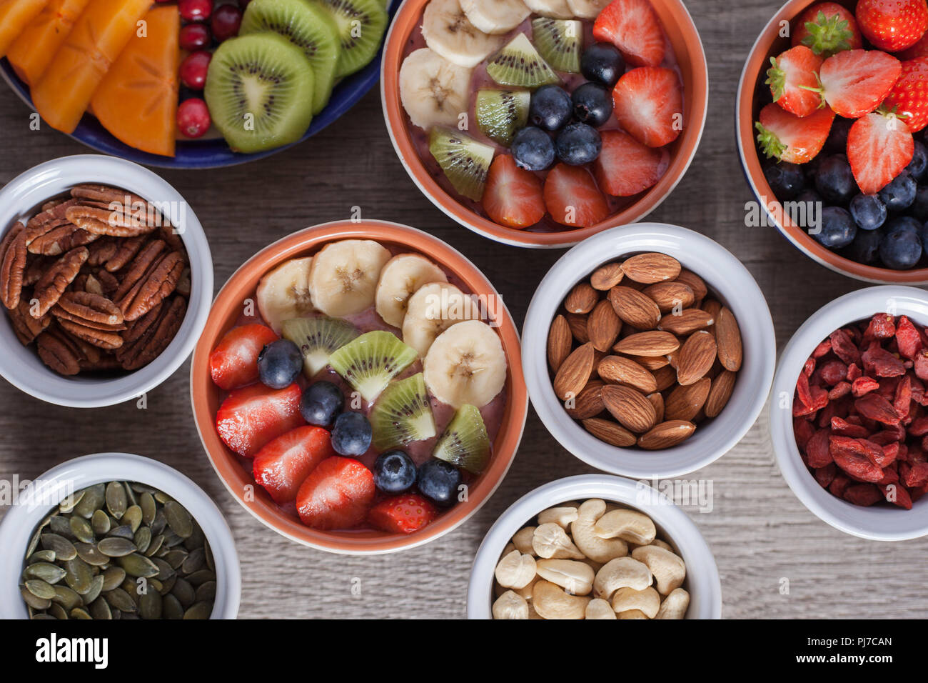 Smoothie mit Früchten und Beeren auf den grauen Holztisch, mit einer Vielzahl von Früchten und Nüssen herum, selektiver Fokus, Ansicht von oben Stockfoto