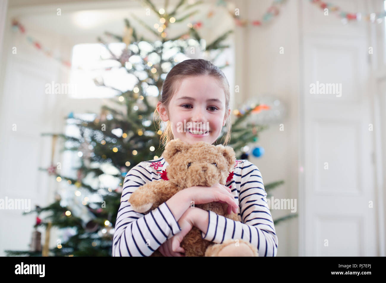 Porträt Lächeln, cute girl Holding Teddybär vor Weihnachtsbaum Stockfoto