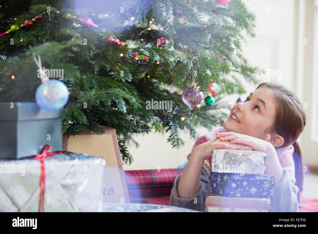 Neugierige Mädchen mit Stapel Geschenke bis an Weihnachten Baum suchen Stockfoto