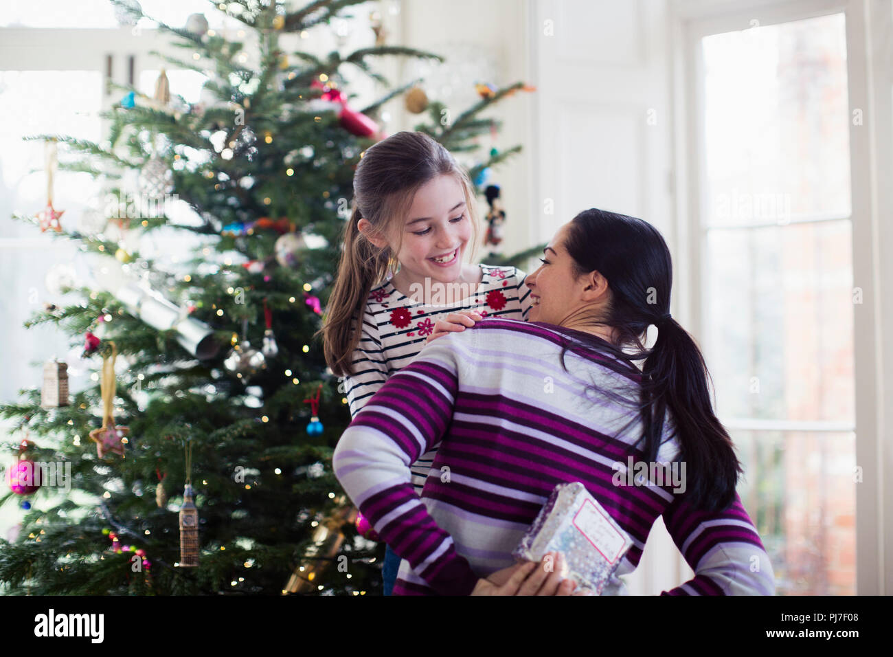 Verspielte Mutter verstecken Weihnachtsgeschenk von Tochter im Wohnzimmer Stockfoto