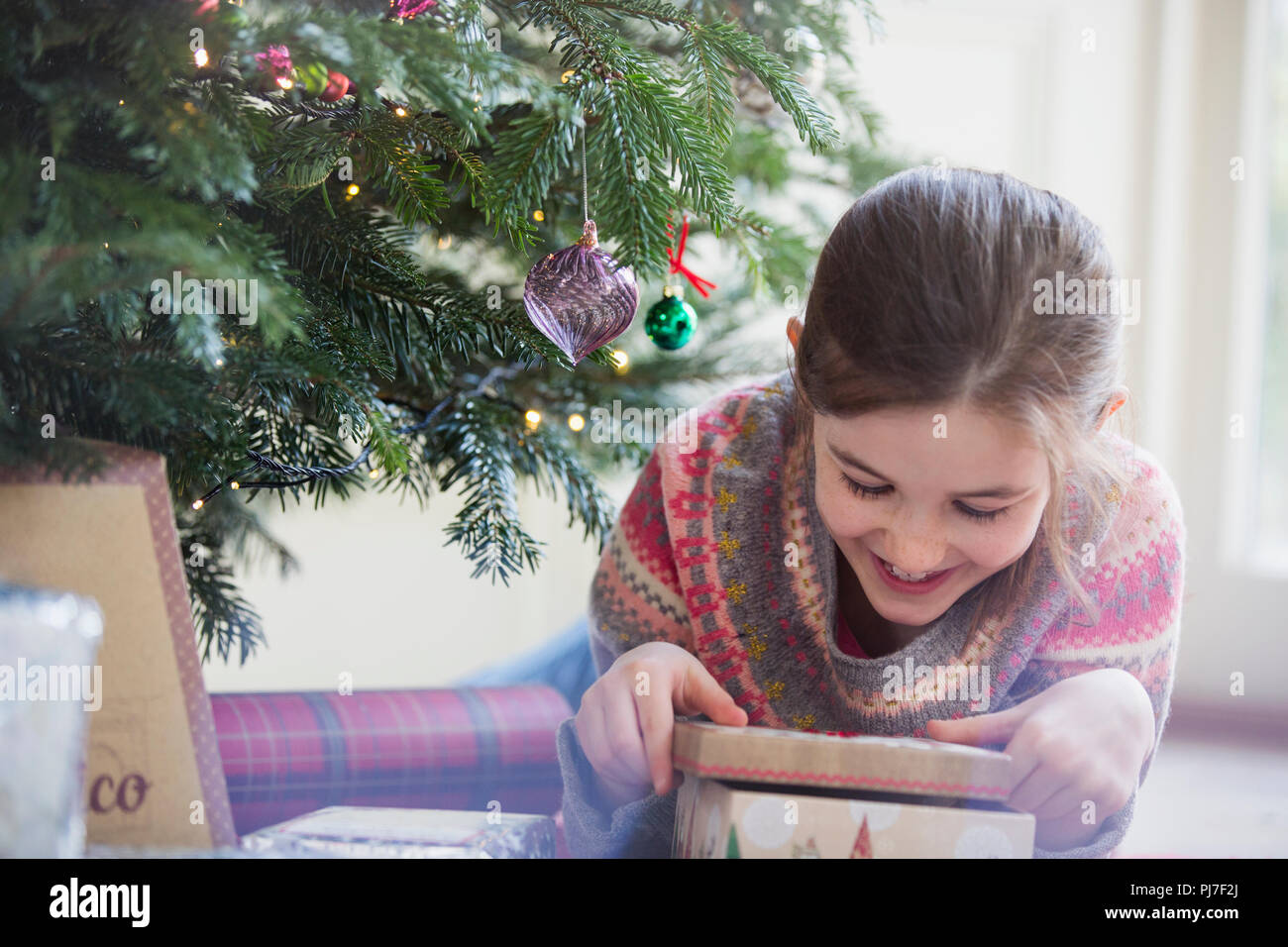 Lächelnd, neugierige Mädchen öffnen Weihnachtsgeschenk Stockfoto