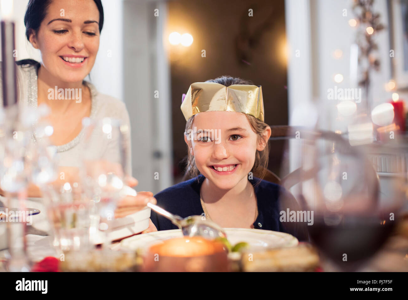 Lächelnde Mutter und Tochter in Papier Krone genießen Weihnachten Abendessen Stockfoto