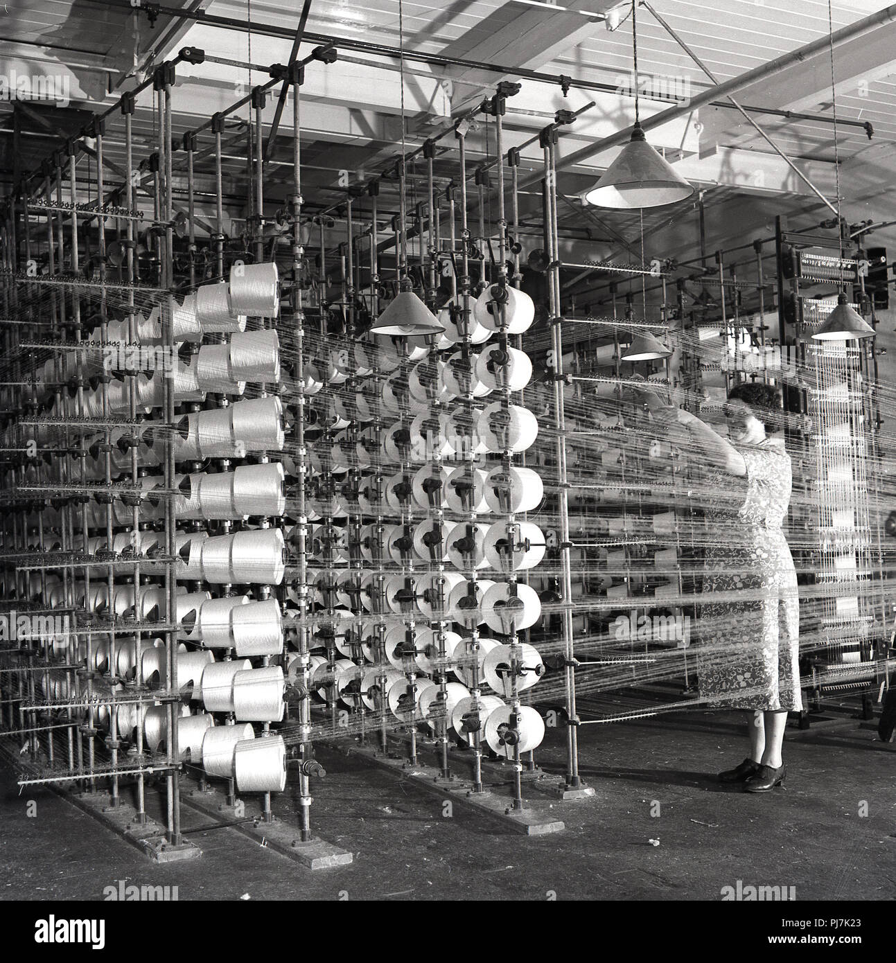 1950er Jahre, historische, Textilherstellung, einem erwachsenen weiblichen Arbeiter in Schürze Kontrolle der Spindeln oder Spulen des Gewindes in einer Textilfabrik, Nordirland, Großbritannien. Stockfoto