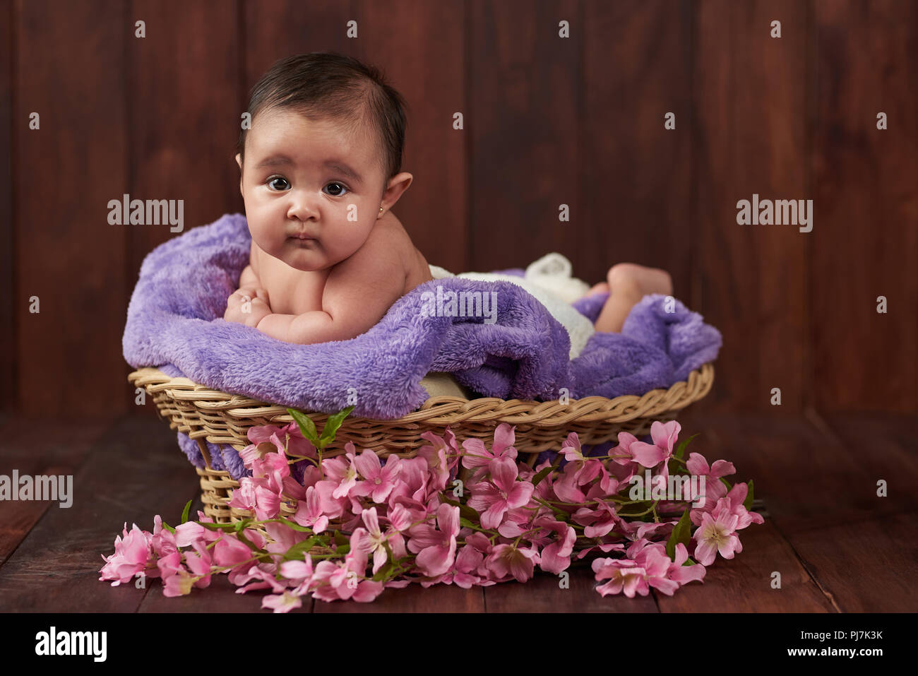 Baby Mädchen legen im Warenkorb sehen Sie die Kamera auf dunklem Hintergrund Stockfoto