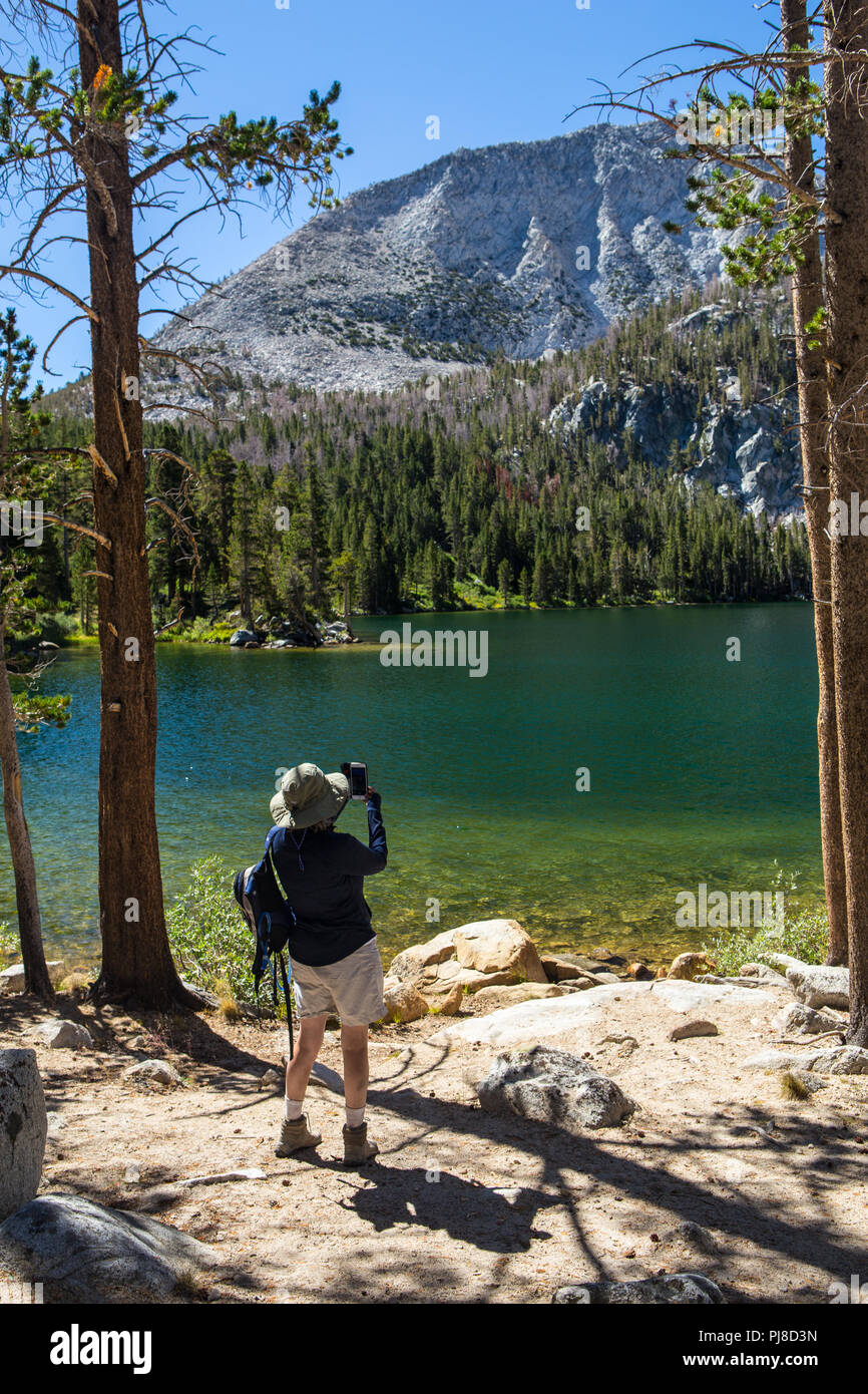 Eine Frau die Bilder mit Ihrem iPhone auf das Hilton Trail Seen in der östlichen Sierra Nevada, Kalifornien, USA Stockfoto