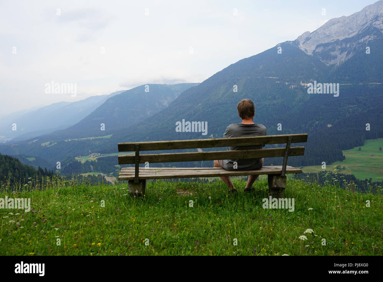 Mann mit Sitzbank mit Blick über das Lesachtal und die Karnischen Alpen, Kärnten, Österreich. Stockfoto