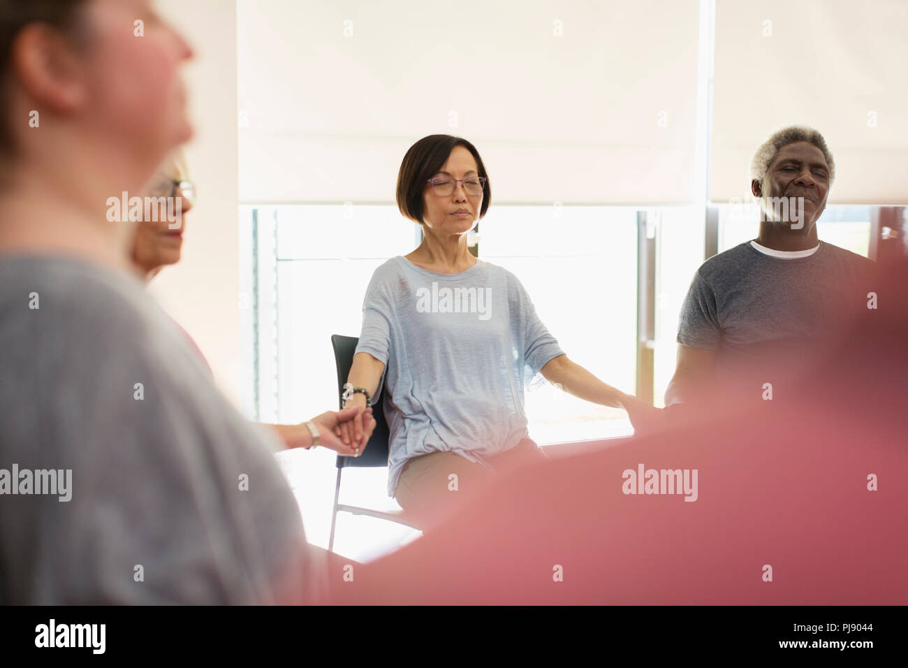 Serene aktive Senioren halten sich an den Händen und Meditieren im Community Center Stockfoto