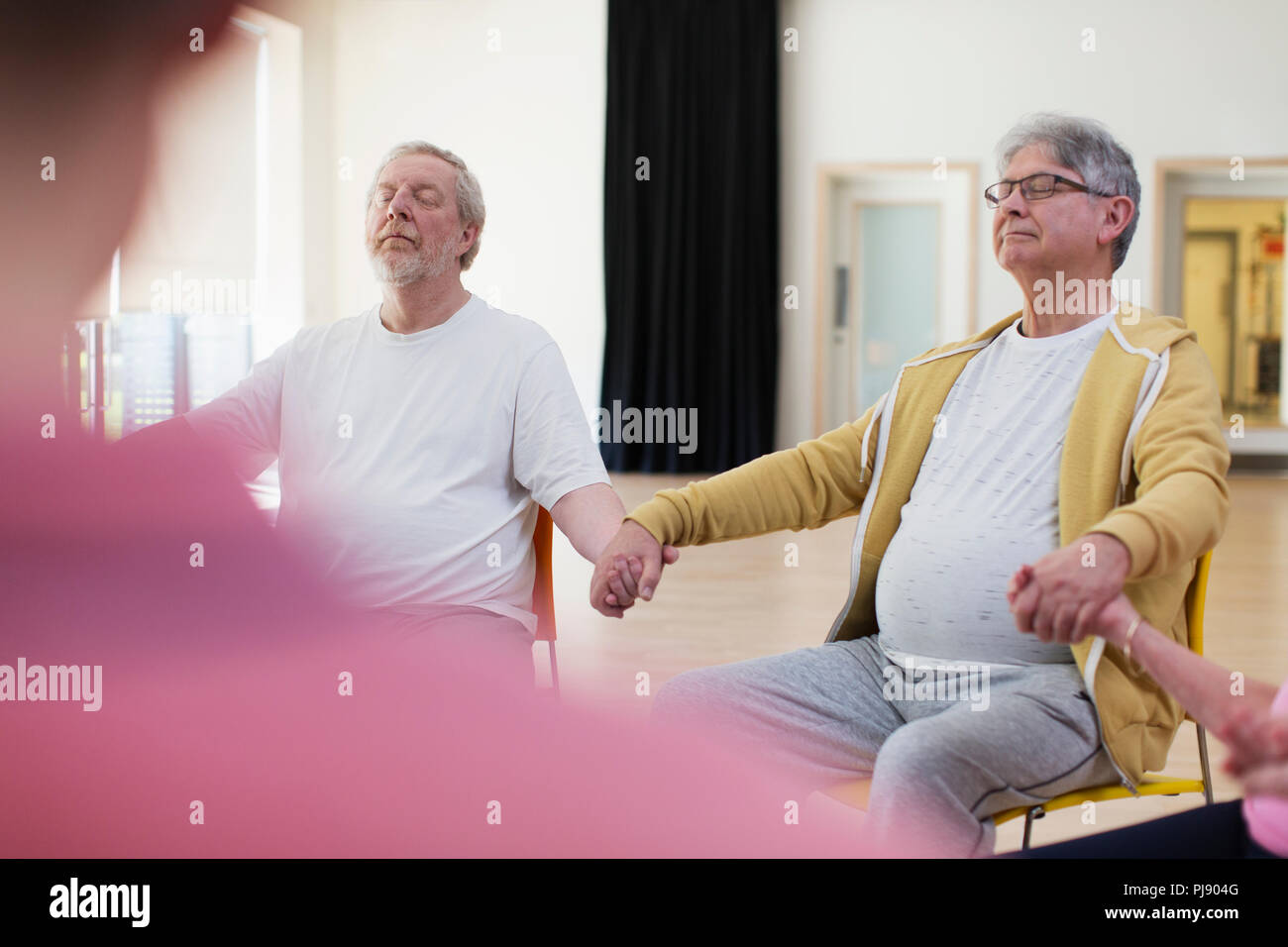 Serene aktive ältere Männer halten sich an den Händen, meditieren im Community Center Stockfoto