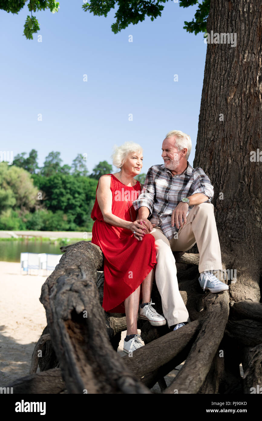 Süße liebevolle Rentnerehepaar sitzen auf großen Baum in der Nähe von wunderschönen Fluss Stockfoto
