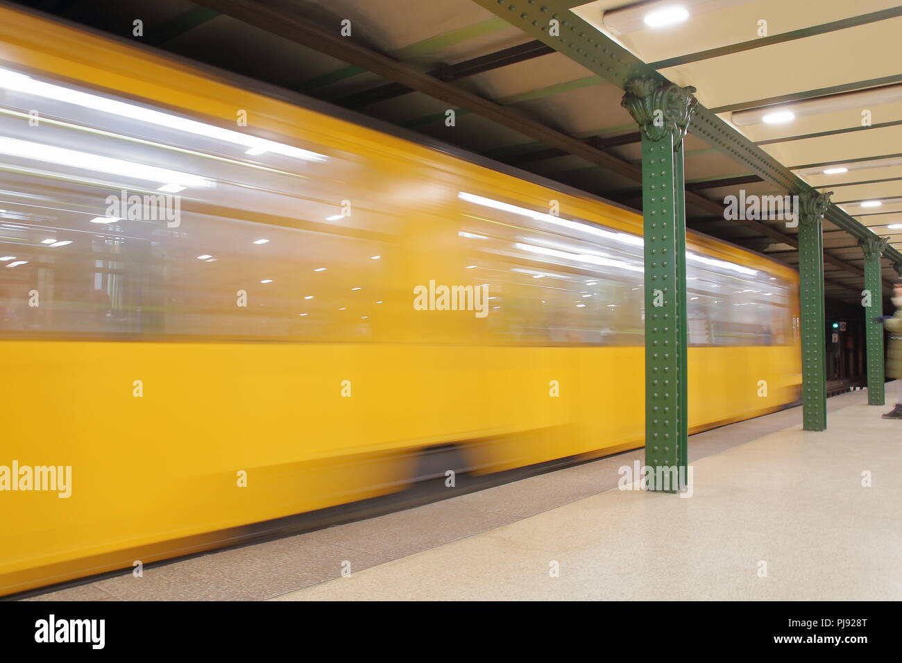 Gelbe Zug fährt u-Plattform, eine Person wartet, Lichter, grün Eisen schöne Säulen. Stockfoto