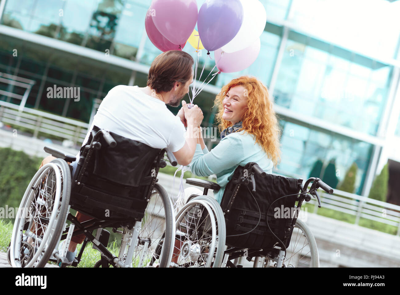 Charmante Mann und Frau im Rollstuhl übertragen, während Sie Ballons Stockfoto
