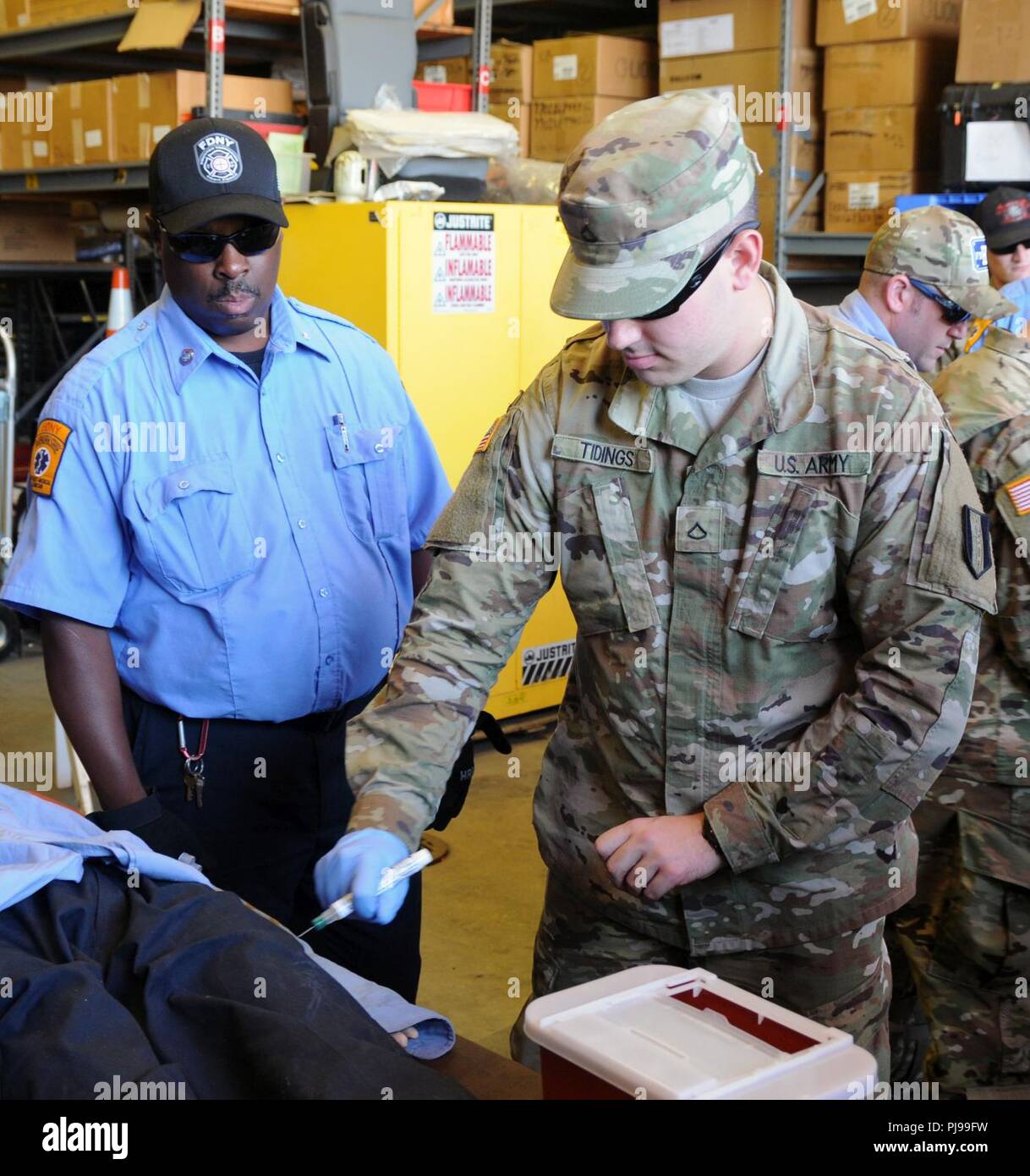 Die Feuerwehr der Stadt New York (FDNY) Feuerwehrmann in das gefährliche Material Unternehmen beobachtet, wie der US-Army Reserve Pfc. Colin verkündigen, 424Th Engineer Company, verwaltet eine DuoDote Injektion zu einer Schaufensterpuppe, als ob er zu einem Nerv Agent an der New York City Feuerwehr (FDNY) Brand Academy auf Randalls Island in New York City, New York, 9. Juli 2018 ausgesetzt war. FDNY mit US-Armee Northern Command (NORTHCOM) leitet die Ausbildung Als gemeinsame Ausübung Simulation von chemischen, biologischen, radiologischen und nuklearen (CBRN) Veranstaltungen die geeignete Antwort auf die ersten Reaktion zu maximieren. Stockfoto