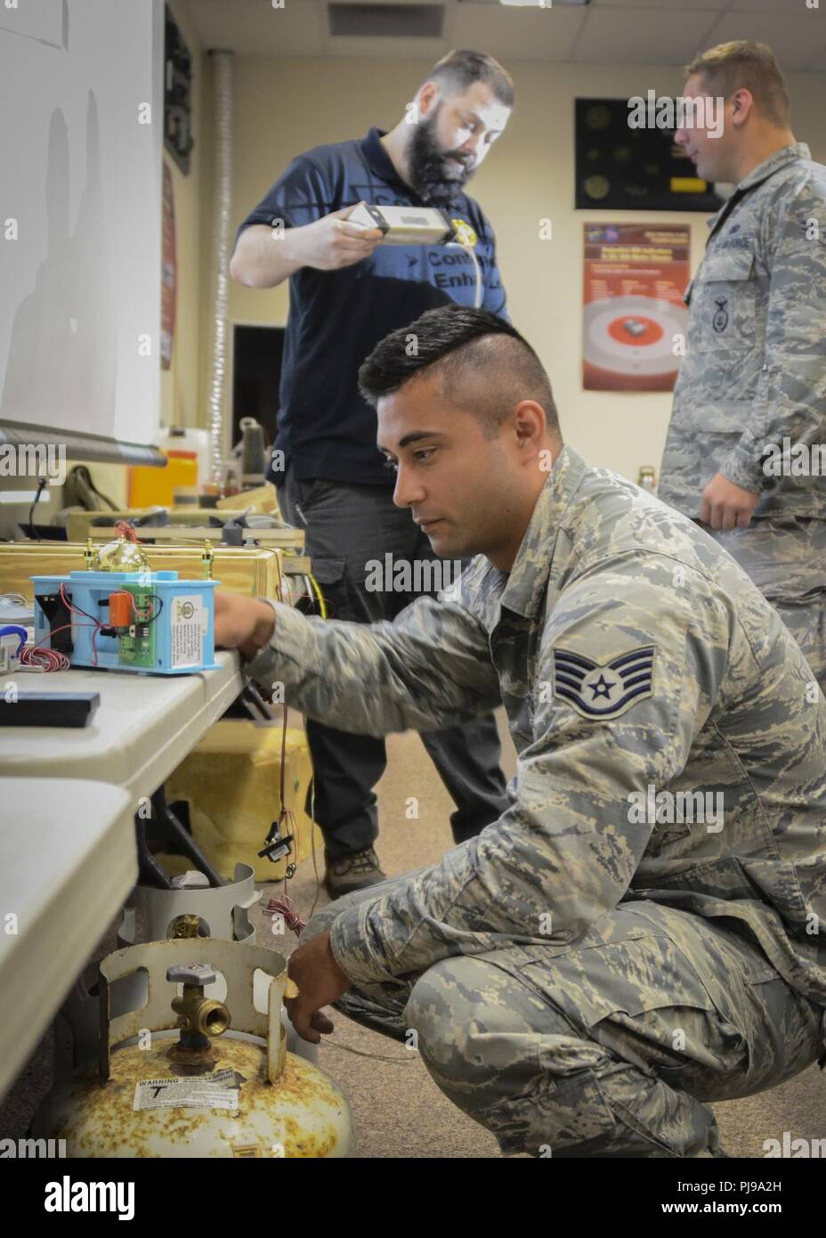 Us Air Force Staff Sgt. Joshua Shearrer, ein Mitglied der Sicherheitskräfte Geschwader mit Die 128 Luftbetankung Flügel, Wisconsin Air National Guard, untersucht ein Dummy Zeitbombe während der Improvised Explosive Device Bewusstsein Kurs am Joint Base Elmendorf-Richardson, Ala., 10. Juli 2018. Die 128 ARW Sicherheitskräfte Flieger angeregt wurden, zu berühren, halten, und untersuchen, Modelle der modernen IEDs wie Wind-up Alarm Clocks, hot-wired cellphones, schnellkochtopf Bomben, und Propan tank Sprengstoff. Moderner IEDs sind tödlich, incognito Gefahren in Umgebungen eingesetzt, aber Bewusstsein Seminare wie zum Beispiel. Stockfoto