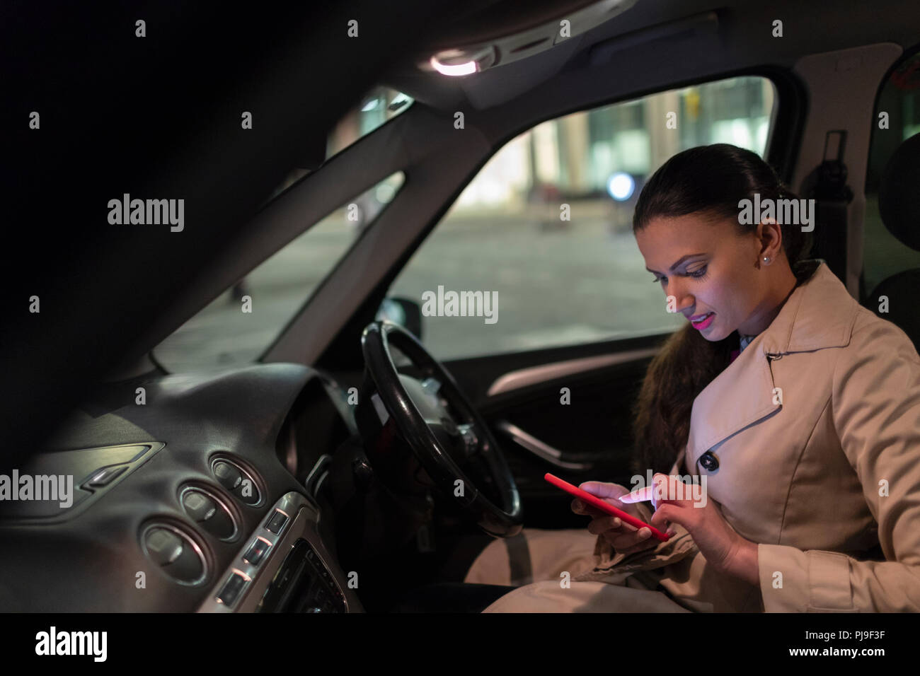 Geschäftsfrau mit smart Telefon im Auto in der Nacht Stockfoto