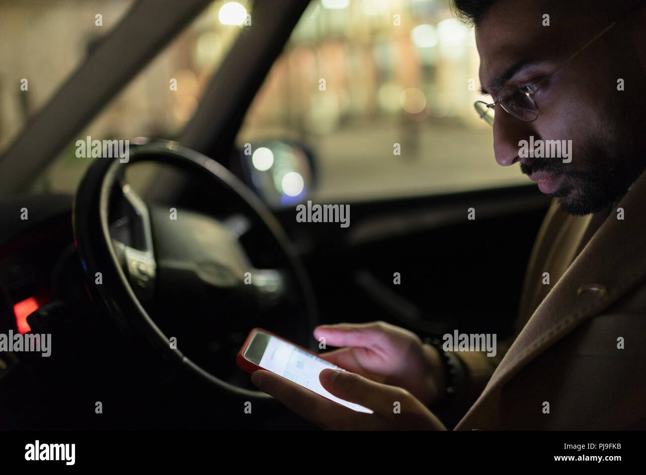 Mann mit smart Telefon im Auto in der Nacht Stockfoto