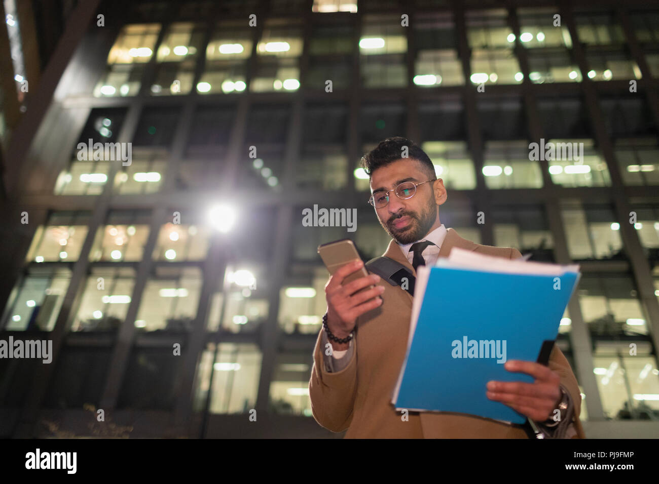 Geschäftsmann mit Papierkram und Smart Phone unter städtischen Hochhaus in der Nacht Stockfoto