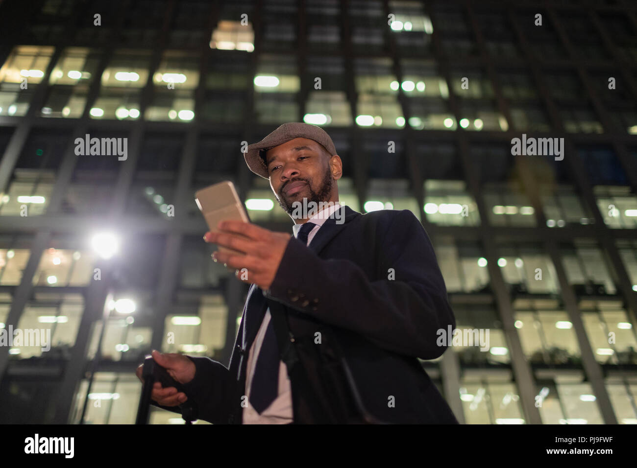Geschäftsmann mit smart phone stehen unter städtischen Hochhaus in der Nacht Stockfoto