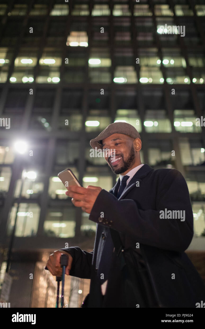 Lächelnd Geschäftsmann mit smart phone stehen unter Hochhaus in der Nacht Stockfoto