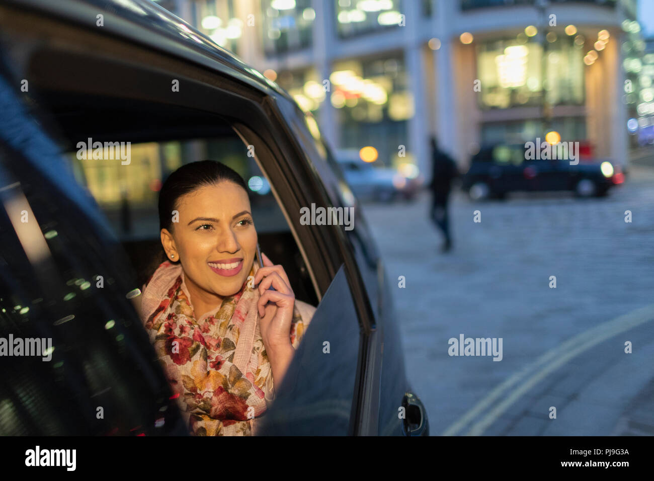 Lächelnd Geschäftsfrau mit smart phone in crowdsourced Taxi in der Nacht Stockfoto