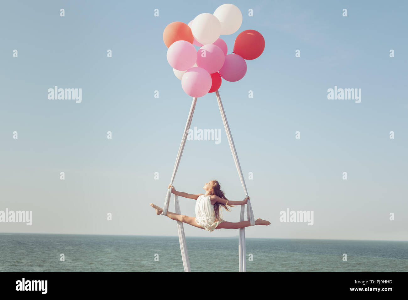 Mädchen macht ein Garn auf der Leinwand über dem Meer. Ballons halten die Leinwand in der Luft. Stockfoto