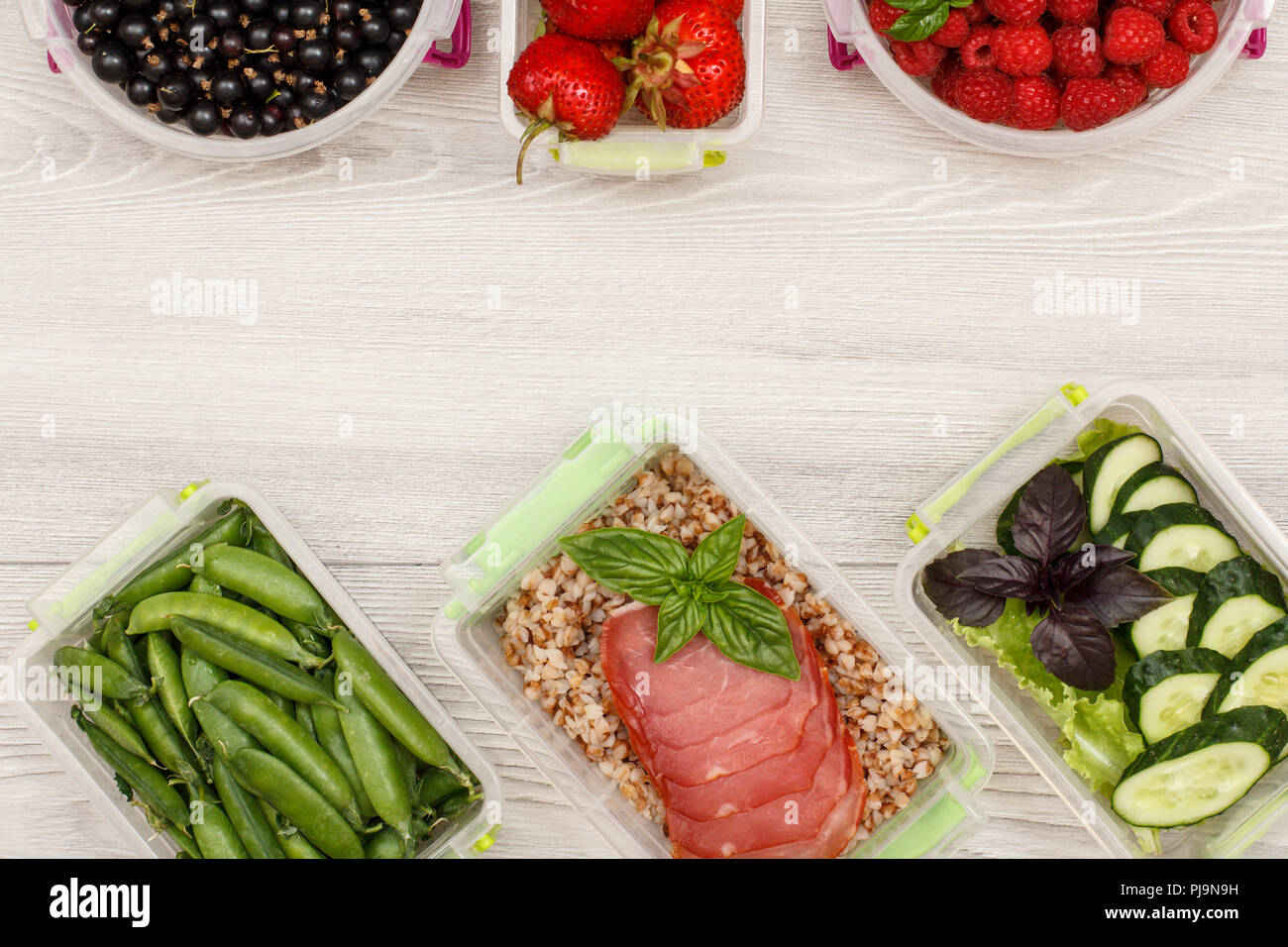 Kunststoff Mahlzeit prep Container grüne Erbsen, mit gekochten Buchweizen Brei und Scheiben von Fleisch, frischen Gurken und Salat, Johannisbeere, Erdbeere, Himbeere Stockfoto
